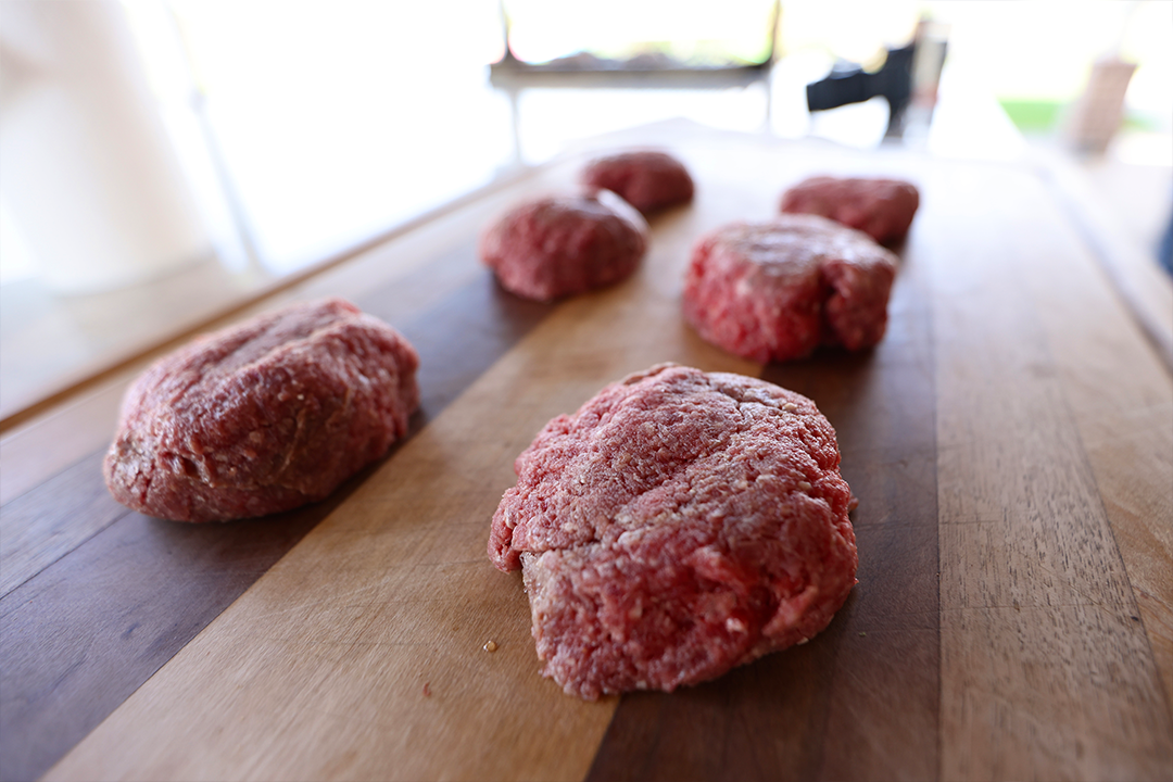 Portions of raw ground beef resting on a wooden board, ready to be shaped into burger patties.