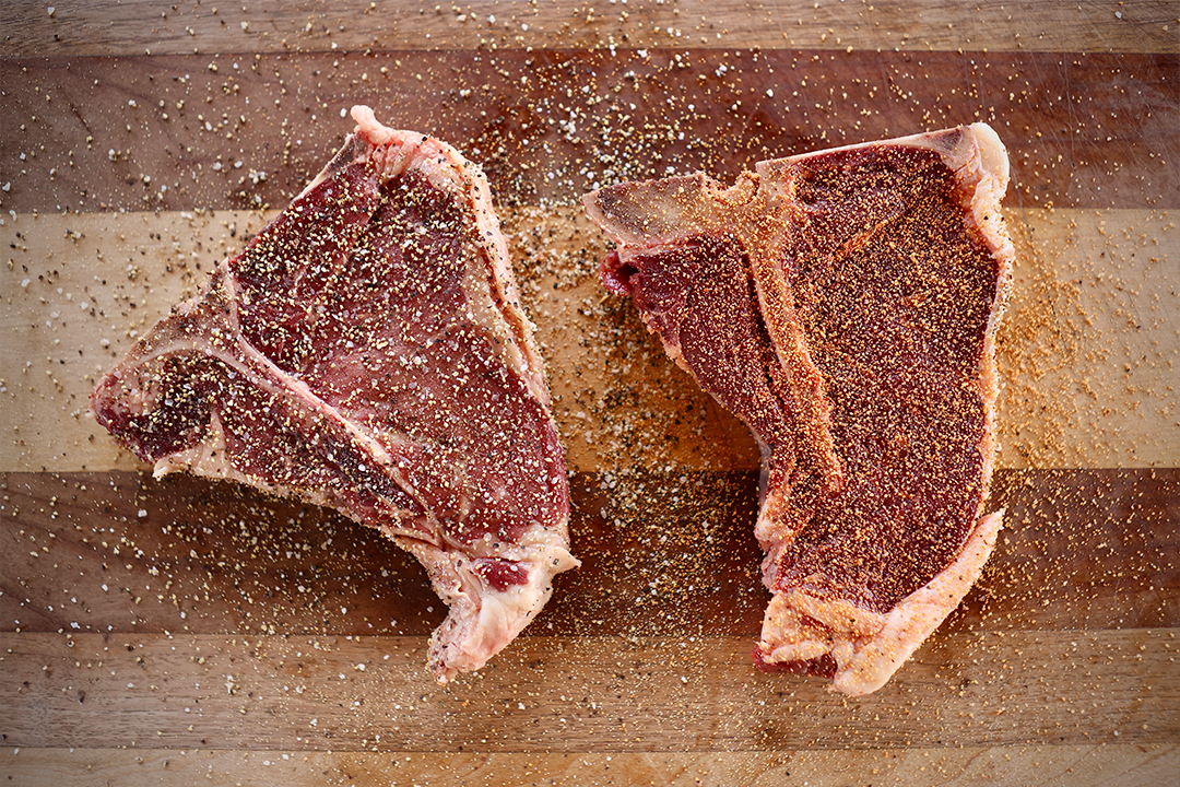 Four well-seasoned hamburger patties cooking over hot coals in a charcoal grill, ready to serve with that classic backyard barbecue flavor.